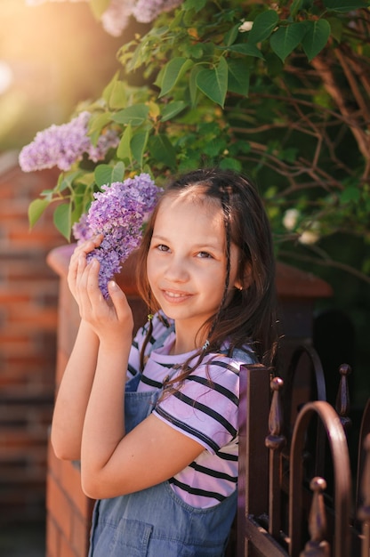 花の咲くリリアックの花を保持している少女の肖像画暖かい春の日に屋外で愛らしい子供の子供垂直