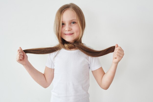 Портрет маленькой девочки, держащей волосы в руках на белом фоне