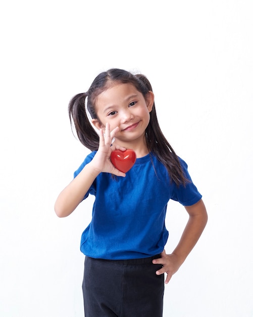 Portrait of little girl holding red heart on white wall. Space for text