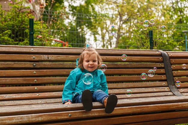 Portrait of a little girl in the park on a bench catches soap bubbles