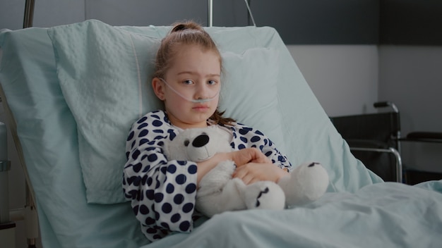 Portrait of little girl patient wearing oxygen nasal tube resting in bed recovery after suffering pn...