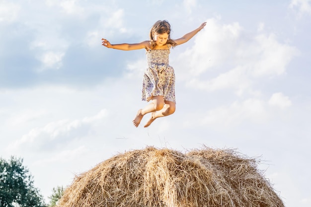 Portrait of little girl playing and jumping on haystack in field High bounce Reach sky Low angle One kid in field