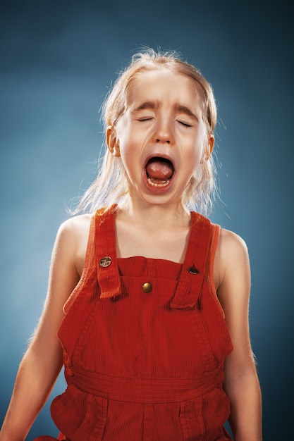 Foto il ritratto di una bambina in abito rosso su sfondo blu. lei sta piangendo