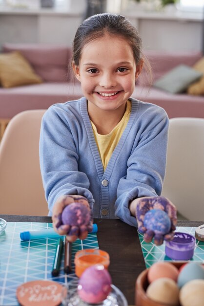 Портрет маленькой девочки, улыбающейся в камеру и показывающей крашеные яйца в руках на праздник Пасхи