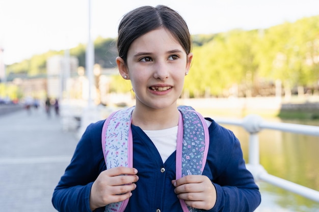 Portrait of little girl smiling looking to the side with school backpack and thoughtful look