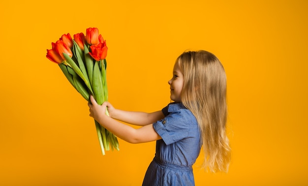 スペースのコピーと黄色の壁に赤いチューリップの花束と横に立っている少女の肖像画