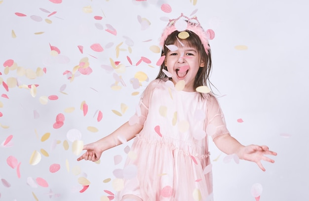 Portrait of little girl wearing pink dress in tulle with princess crown on head isolated on white background enjoy confetti surprise Happy playful girl celebrating her birthday party having fun