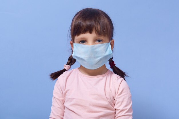 portrait of little girl wearing roseshirt and disposable mask on her face, posing