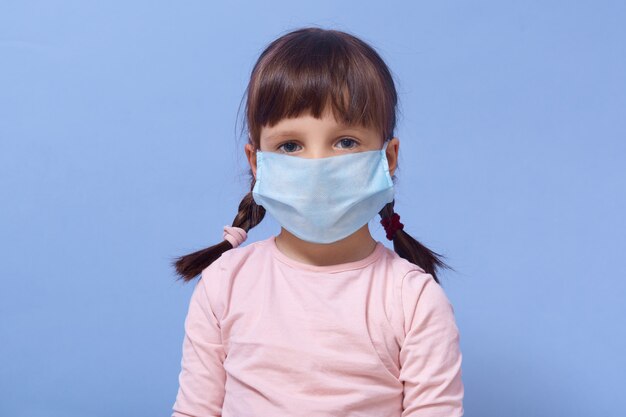 Portrait of little girl wearing roseshirt and disposable mask on her face, posing