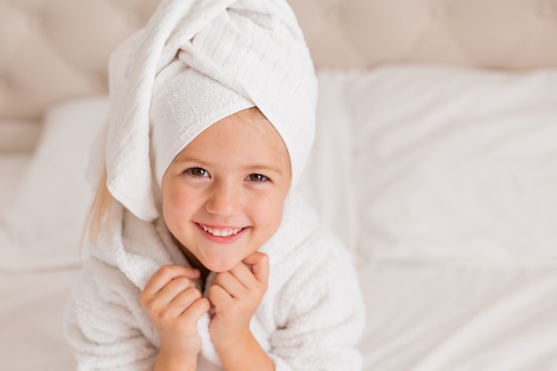 portrait of a little girl in a white bathrobe with a white towel on her head lying in bed