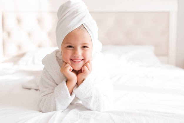 portrait of a little girl in a white bathrobe with a white towel on her head lying in bed