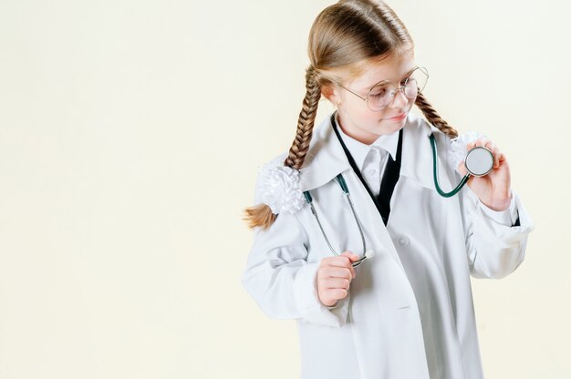 Portrait of a little girl in a white doctor s coat with glasses, documents and a stethoscope who looks at the camera and smiles.