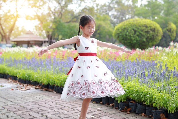 庭の周りの花でリラックスした白いドレスの少女の肖像画。