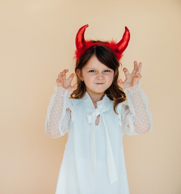 Portrait of a little girl in a white dress with devil horns Halloween costume Angry mood A menacing expression on his face