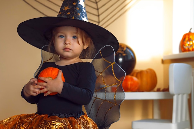 Photo portrait of a little girl in a witch costume with a pumpkin in her hands