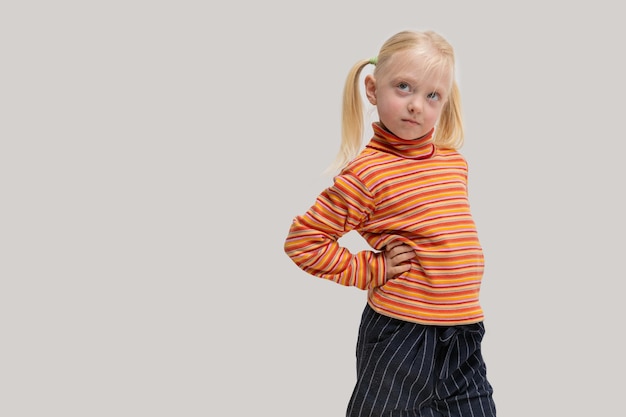 Portrait of a little girl with blond hair in an orange striped shirt and black trousers