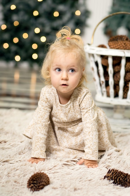Portrait of a little girl with blonde hair in a photo of a Christmas tree and New Year's decor on the eve of Christmas