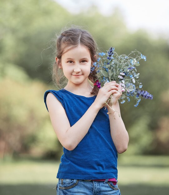 Photo portrait of a little girl with a bouquet of wild flowers.