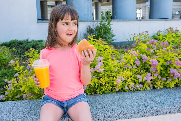 A portrait of a little girl with a cheeseburger and orange juice Fast food