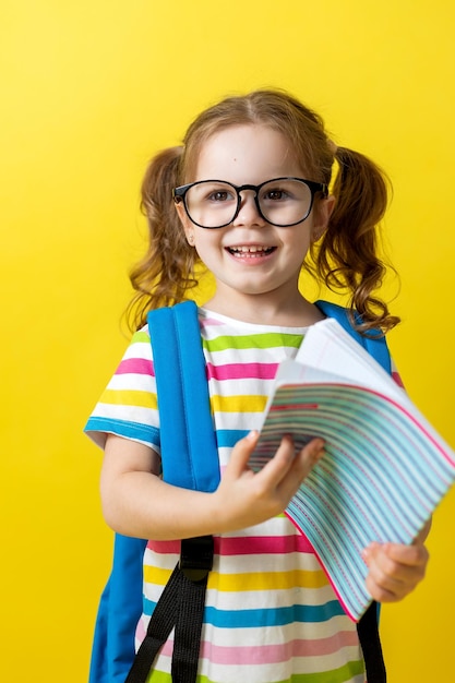 Photo portrait of little girl with glasses in a striped tshirt with notebooks and textbooks in her hands