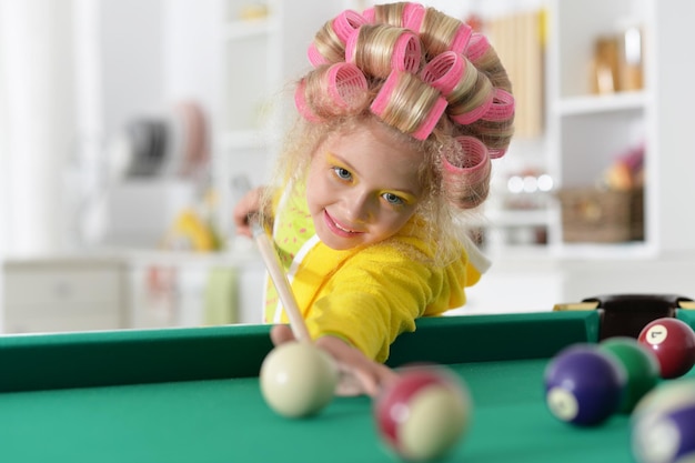 Portrait of little girl with hair curlers playing billiard