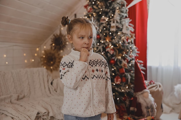 Portrait of a little girl with a lollipop at the Christmas tree in the New Year's decorated room