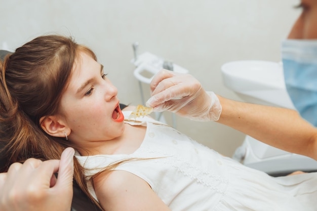 Portrait of a little girl with an open mouth sitting in a dentist's chair while an orthodontist holds a plate on her teeth Dentist puts a plate in a child's mouth