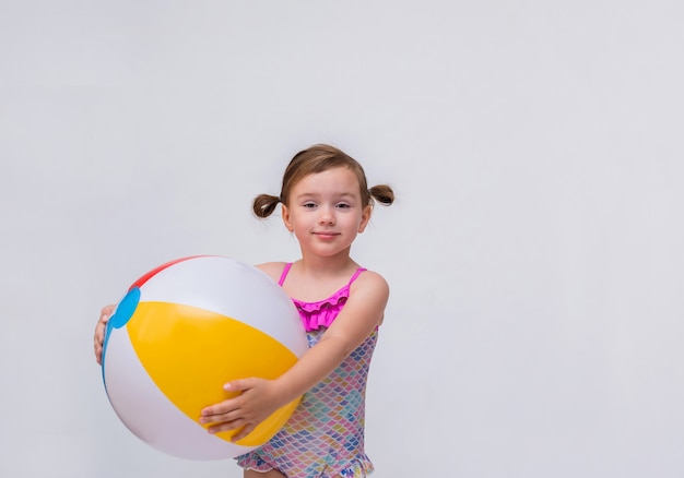 Portrait of a little girl with ponytails in a swimsuit with an inflatable ball on a white isolated