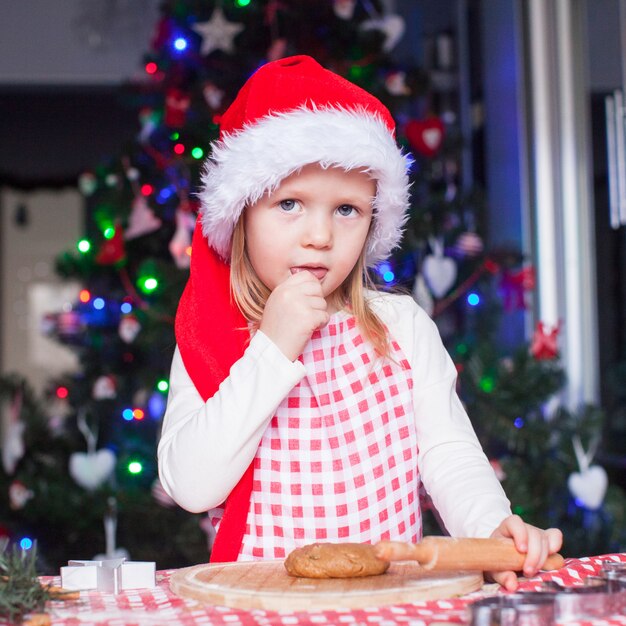 Portrait of little girl with rolling pin baking gingerbread cookies for Christmas