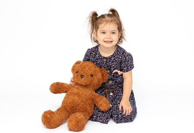 Portrait of little girl with teddy bear on white surface