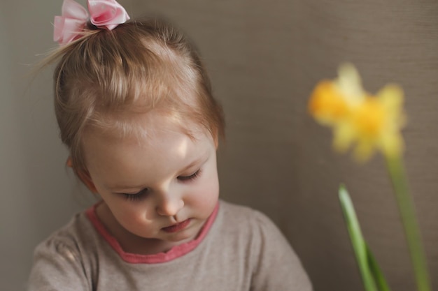 Ritratto di una bambina con fiore di narciso primaverile giallo a casa