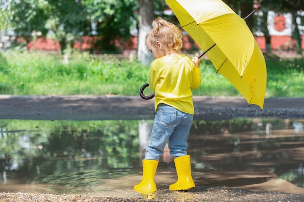 Portrait of a little girl in yellow clothes and with a bright yellow umbrella in her hands