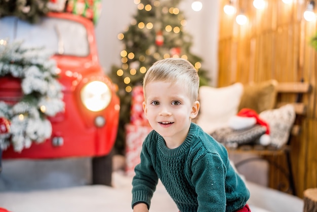Портрет маленького счастливого мальчика против машины с венком, боке, рождественскими елками с гирляндами огней