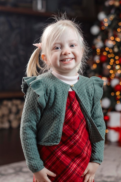 Portrait of little jolly blonde girl in festive new year clothes traditional xmas decorated living room Vertical frame