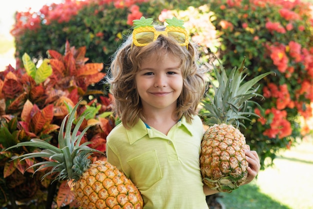 Portrait of little kid outdoors in summer smiling cute funny boy holding a pineapple