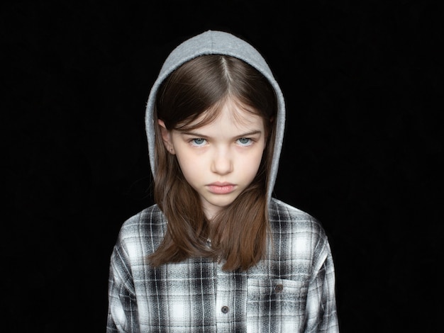 Портрет маленькой обиженной слезливой девушки в толстовке с капюшоном на черном