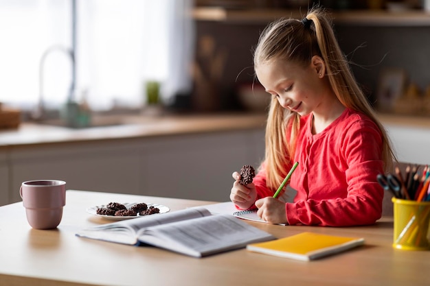 Photo portrait of little schoolgirl having snacks while doing homework