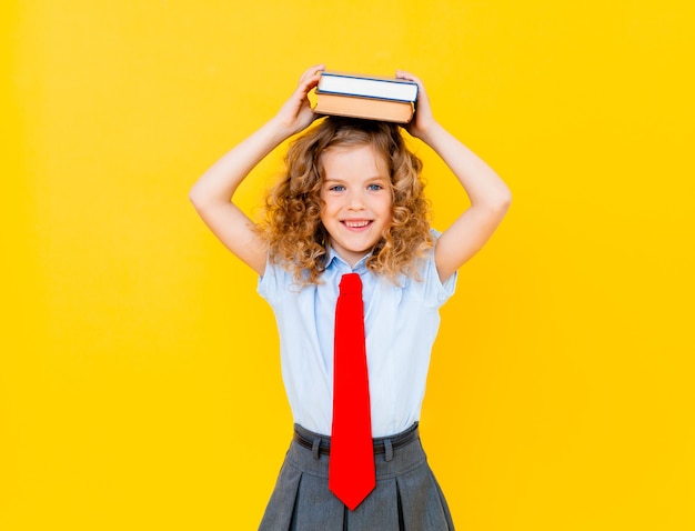 彼女の頭の上に本を持っている小さな女子高生の肖像画。孤立した背景。教育の概念。