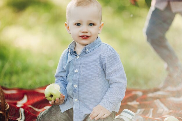 Portrait of little stylish blonde boy among grass and holding apple
