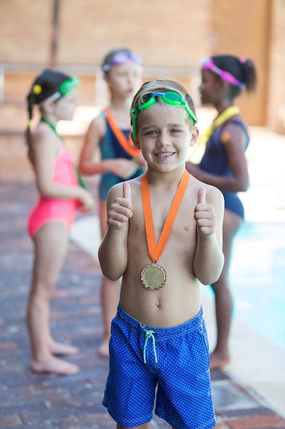 Portrait of little swimmer showing thumbs up at poolside