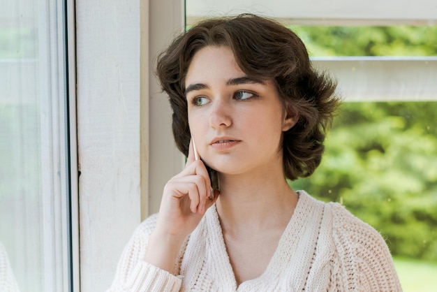 Portrait lonely saucasian young woman sitting near window with phone in he