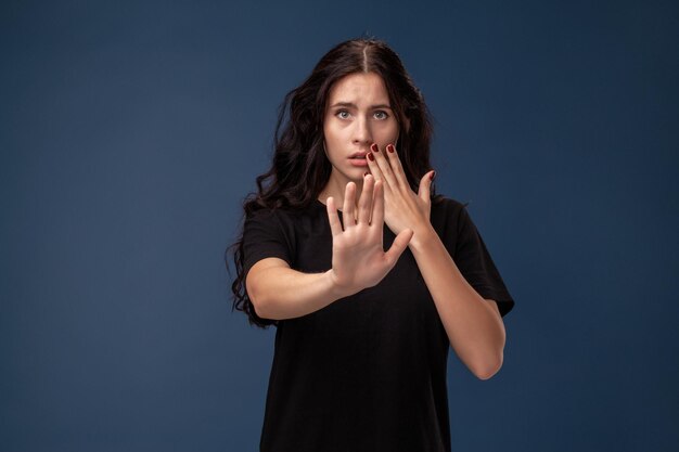 Portrait of a long-haired brunette woman in black t-shirt posing on a gray background and showing different emotions.