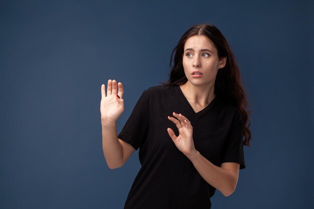 Portrait of a long-haired brunette woman in black t-shirt posing on a gray background and showing different emotions.