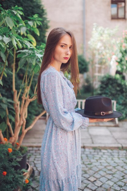 portrait of long haired brunnette girl in blue dress holding hat in her hands