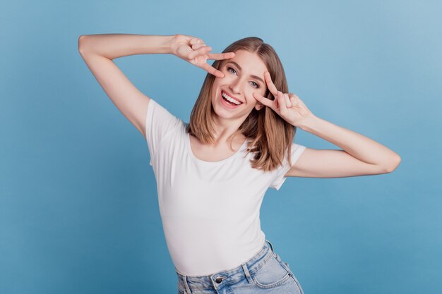 Portrait of lovely adorable lady show v-sign close eyes have fun party concept on blue background