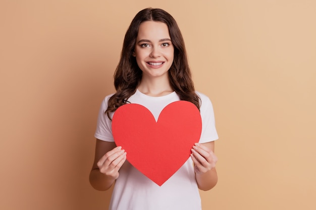 Portrait of lovely affectionate girl hold big red paper heart isolated on beige background