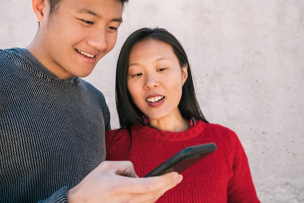 Portrait of lovely asian couple looking at the mobile phone while spending good time together. Love and technology concept.