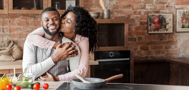 portrait of lovely black couple embracing at kitchen