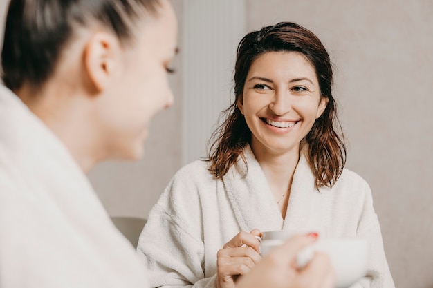 Portrait of a lovely caucasian brunette smiling while looking at her girlfriend relaxing after spa procedures in their body .