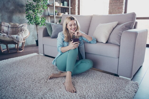 Portrait of lovely charming cheerful lady sitting on carpet hold phone